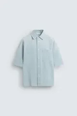 Camisa de corte relajado confeccionada en tejido de algodón, con estampado de cuadros pequeños en tonos celestes y blancos. Presenta cuello solapa, manga corta y bolsillo plastrón en el pecho con cierre frontal de botones.