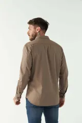 Camisa de hombre color beige con efecto stone wash, corte regular, cuello clásico, cierre frontal con botones, dos bolsillos con solapa abotonada en el pecho y mangas largas con puños abotonados.