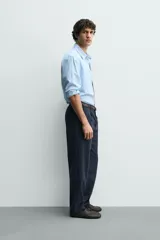 Pantalón de corte recto confeccionado en tejido elástico, con cintura elástica, pliegues frontales, bolsillos laterales y bolsillos traseros de vivo con botón.