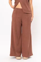 Pantalón de corte ancho y tiro alto, confeccionado en tejido de punto color marrón. Presenta cintura elástica y costuras verticales decorativas en el frente de cada pierna.
