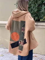 Campera tipo hoodie confeccionada en tejido de corderito color camel, con diseño de collage en la espalda que combina parches de tela en tonos verde oliva, naranja y estampados étnicos. Presenta un corte holgado y capucha integrada.