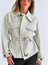 Campera blanca de algodón con cuello amplio, bolsillos delanteros con solapa, mangas largas y cinturón ajustable con hebilla redonda oscura. Cuenta con botones negros a contratono.