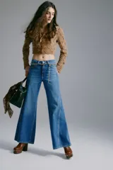 Jean de tiro alto y corte acampanado, confeccionado en denim de algodón. Presenta diseño de cinco bolsillos, cierre frontal con botón y costuras decorativas laterales.