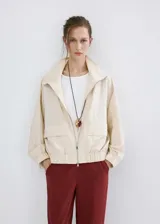 Chaqueta oversize color beige con cuello alto, cierre frontal de cremallera, bolsillos frontales con solapa y mangas largas.