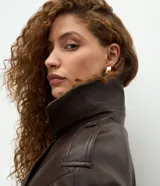 Campera de cuero sintético color marrón oscuro, con diseño de cuello blazer, cierre frontal cruzado, mangas largas estructuradas y ruedo con elástico fruncido.