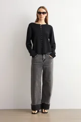 Chaqueta de tejido de punto color negro, con cuello redondo y cierre frontal mediante alamares metálicos. Presenta mangas largas con puños rectos y un corte recto.