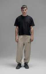 Pantalón deportivo de microfibra color beige, con corte regular y diseño de inspiración vintage. Presenta vivos laterales a contratono, cintura elástica y puños elásticos en los tobillos.