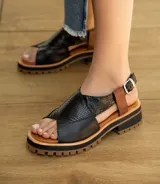 Sandalia de cuero vacuno color negro, con suela de goma deportiva, hebilla al tobillo y horma ancha.