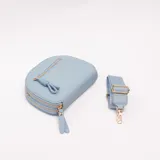 Bandolera celeste de cuero sintético con diseño semicircular, doble compartimento con cierre y bolsillo frontal con tirador decorativo en forma de lazo. Cuenta con herrajes dorados y correa ajustable y desmontable.