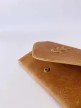 Billetera tipo sobre confeccionada en cuero color camel, con solapa en punta y detalle de costura decorativa en forma de espiga. Cuenta con cierre de broche y monedero externo.