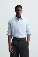 Camisa de manga larga color celeste claro, corte regular fit, con cuello solapa, bolsillo plastrón en el pecho y cierre frontal de botonadura.