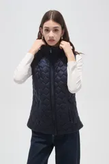 Chaleco acolchado negro con diseño de costuras geométricas, cierre frontal completo y bolsillos laterales.