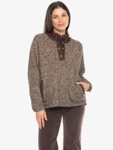Sweater de tejido grueso jaspeado en tonos marrones y beige, con cuello alto de pana marrón oscuro y cierre frontal parcial con botones a presión. Posee un bolsillo canguro en la parte delantera.