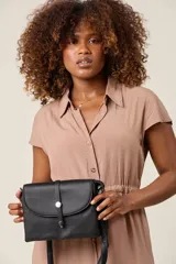 Bandolera negra de ecocuero con correa ajustable y solapa con cierre de botón metálico.