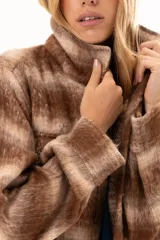 Chaqueta de textura suave y afelpada con diseño de rayas horizontales en tonos beige y marrón. Presenta cuello camisero, cierre frontal con botones y mangas largas con puños abotonados.