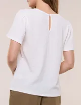 Blusa blanca de textura gofrada, de corte recto y semi holgado, con mangas cortas y escote redondo adornado con un canesú frontal en crochet calado.