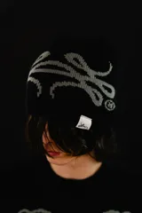 Beanie reversible tejido en algodón, con diseño gráfico abstracto. Presenta un lado en color negro con estampa gris y el otro lado en color gris con estampa negra. Incluye etiqueta de marca en el borde inferior.