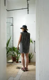 Vestido corto de jean color gris oscuro con efecto acid wash, sin mangas, con cuello camisero y cierre frontal de botones. Incluye dos bolsillos en el pecho con solapa y pespuntes decorativos.