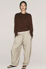 Pantalón de tiro medio con diseño de cuadros vichy en tonos neutros. Presenta pierna ancha, cintura elástica ajustable con cordones, bolsillos laterales y detalle de pinzas en el delantero.