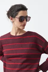 Sweater de tejido de punto con diseño de rayas horizontales en tonos bordó y rojo. Presenta cuello redondo, mangas largas con hombros caídos y terminaciones acanaladas en puños, cuello y ruedo.