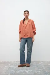 Camisa de corte holgado en color ocre, con escote en V y cordones con borlas decorativas. Presenta mangas largas abullonadas con puños elásticos y un diseño de textura rústica.