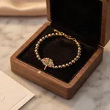 Pulsera de acero con baño de oro, compuesta por esferas doradas y oscuras, con un dije central en forma de árbol de la vida decorado con cristales multicolores.