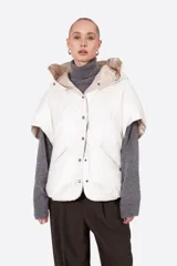 Campera tipo capa acolchada de color blanco, estilo plumífero. Presenta un diseño sin mangas, cuello alto con capucha y cierre frontal mediante botones a presión dorados. Confeccionada en tejido de nylon con relleno térmico.