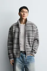 Chaqueta de punto con diseño de rayas horizontales en tonos grises, cuello subido y cierre frontal de cremallera completa. Presenta un corte relajado y acabados en rib en puños y bajo.