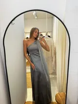 Vestido largo de tafeta con brillo, color verde, de corte al cuerpo y escote asimétrico de un solo hombro. Incluye una pieza de seda liviana drapeada sobre el hombro opuesto.