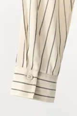Camisa de corte recto confeccionada en mezcla de algodón y viscosa, con estampado de rayas verticales. Presenta cuello solapa, cierre frontal con botones y mangas largas con aplicaciones de encaje y bordados a tono.