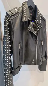 Campera estilo motoquera de símil cuero negro, con solapas amplias y detalles de tachas metálicas en solapas, hombros y mangas. Presenta cierre frontal cruzado, bolsillos con cierre y trabillas en el ruedo.