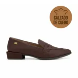Zapato tipo mocasín de cuero negro con taco bajo cuadrado y detalle de aplique metálico dorado en el lateral.