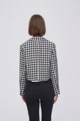 Blazer corto de poliéster con diseño a cuadros en blanco y negro, cuello solapa y cierre frontal de doble botonadura.