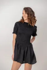 Vestido corto de color negro, con cuerpo y mangas cortas de nido de abeja fruncido, y falda corta con vuelo.