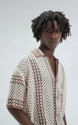 Camisa de manga corta tejida en punto abierto (símil crochet), color beige con detalles en marrón. Presenta cuello solapa, cierre frontal con botones y calce oversize.