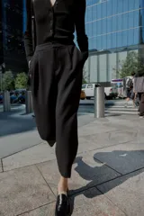 Pantalón de tiro medio con pinzas delanteras, bolsillos laterales y falsos bolsillos de vivo en la parte trasera. Presenta un corte holgado que se estrecha hacia el tobillo, con bajo acabado en pliegues y cierre frontal con cremallera, botón interior y gancho.