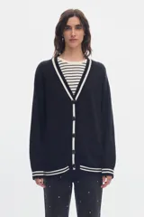 Cardigan de punto negro con diseño estilo varsity, escote en V y cierre frontal de botones. Presenta líneas blancas en contraste a lo largo de la botonera, el escote, los puños y el ruedo.