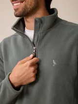 Sweater de polar color beige, con cuello alto y cierre frontal parcial. Presenta un pequeño logo bordado en el pecho.