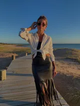 Vestido midi negro de cuero sintético, con escote recto, corte a la cintura y falda recta con flecos.