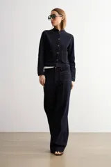 Chaqueta de jean azul oscuro, de corte corto y recto, con cuello mao, cierre frontal de botones metálicos tipo ojal y bolsillos frontales aplicados. Cuenta con costuras pespunteadas en contraste.