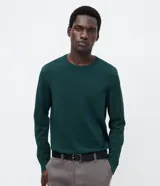 Suéter de punto color verde oscuro, con cuello redondo y mangas largas. Presenta un diseño de corte regular con puños y bajo acanalados, confeccionado en una mezcla de viscosa y poliamida.