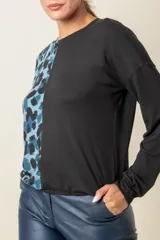 Buzo de manga larga con cuello redondo, combinado en dos tonos: negro liso en la mitad derecha y estampado animal print blanco y negro en la mitad izquierda.