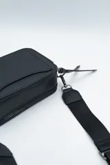 Bandolera de diseño rectangular en color negro, confeccionada en material texturizado. Cuenta con una correa de hombro ajustable y extraíble, cierre superior y tiradores laterales decorativos.