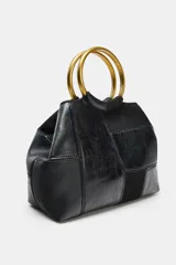 Bolso tipo saca en formato mini con diseño de patchwork en tonos marrones. Cuenta con una anilla metálica rígida como asa de mano y una correa bandolera extraíble. El cierre principal es mediante imán e incluye un bolsillo interior con cremallera.