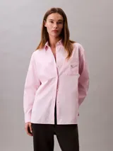 Camisa de corte relaxed confeccionada en popelina de algodón con elastano. Presenta cuello de punta clásico, cierre frontal con botones, mangas largas y un bolsillo en el pecho con el monograma CK bordado en relieve.