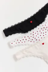 Pack de tres bombachas tipo colaless con terminaciones de encaje. Incluye una unidad negra con un corazón bordado, una unidad blanca con estampado de corazones rojos y una unidad beige con un corazón bordado.