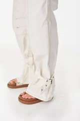 Jean tipo baggy color marrón, de pierna recta y ancha, con cortes circulares, bolsillos laterales y traseros, y tiras ajustables con hebilla en los tobillos.