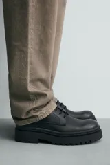 Zapato de vestir tipo derby, color negro, con parte superior lisa, horma redonda, suela con plataforma y piso track.