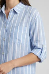 Camisa de manga larga con diseño de rayas verticales en tonos beige y blanco, cuello camisero, cierre frontal con botones y un bolsillo aplicado en el pecho.