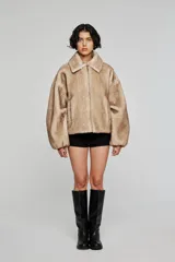 Campera corta de pelo sintético en color beige, con diseño de volumen amplio, cuello clásico, cierre frontal con cremallera y bolsillos laterales integrados.